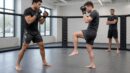 Two fictional MMA athletes demonstrate stance and a compact low check in a training cage