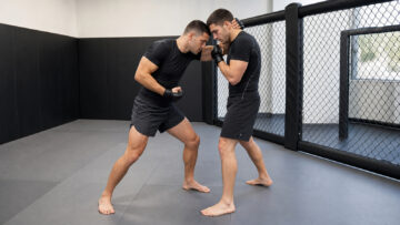 Two generic MMA trainees demonstrate clinch control beside a padded training cage
