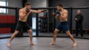 Two fictional MMA athletes test range with a coach observing from outside the training cage